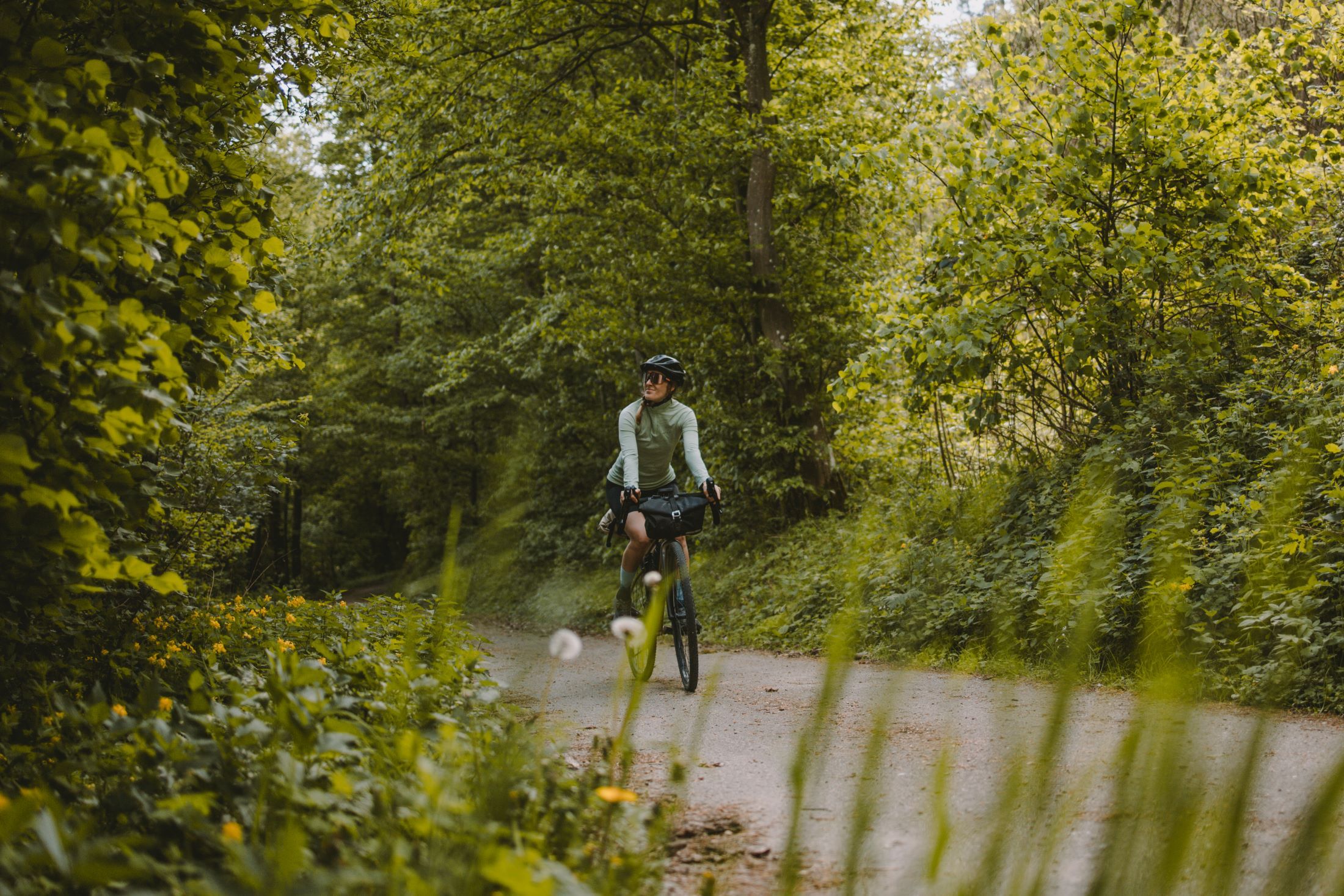 Person auf einem Fahrrad auf einem Waldweg, umgeben von grüner Vegetation.