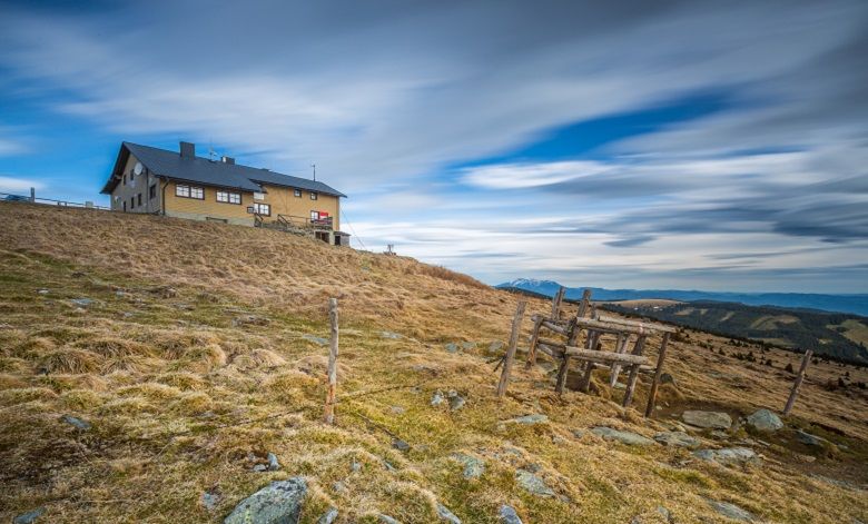Berghütte auf einem Hügel mit bewölktem Himmel im Hintergrund.