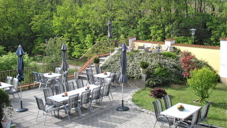 Gästeterrasse mit Tischen, Stühlen und Sonnenschirmen, umgeben von grüner Vegetation.