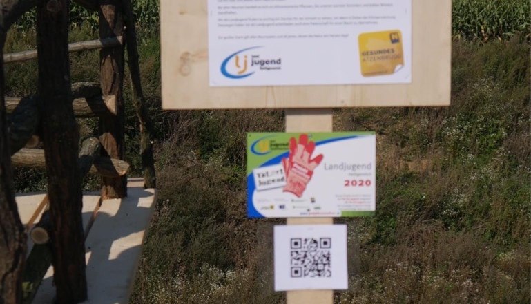 Holzschild mit Informationen zum Baumlehrpfad Atzenbrugg, umgeben von Natur.