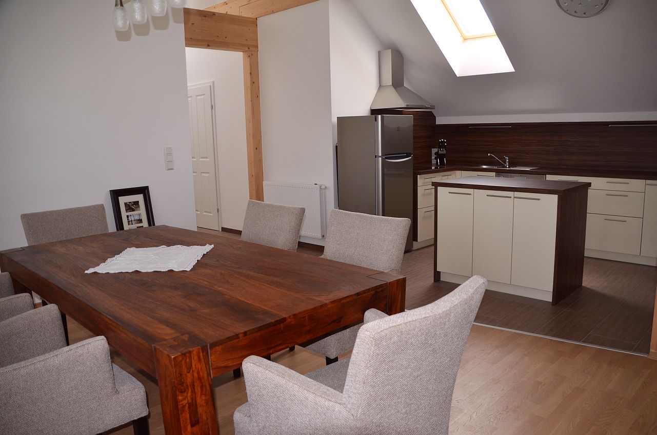 Moderner Essbereich mit Holztisch und grauen Stühlen, angrenzend an eine Küche mit Insel und Dachfenster.