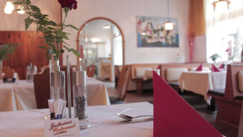 Innenansicht eines gem&uuml;tlichen Restaurants mit gedeckten Tischen, roten Servietten und einer Rose in einer Vase.