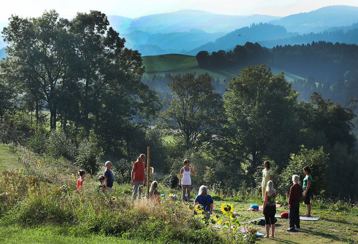 Gruppe von Menschen macht Yoga im Freien vor einer malerischen Berglandschaft.
