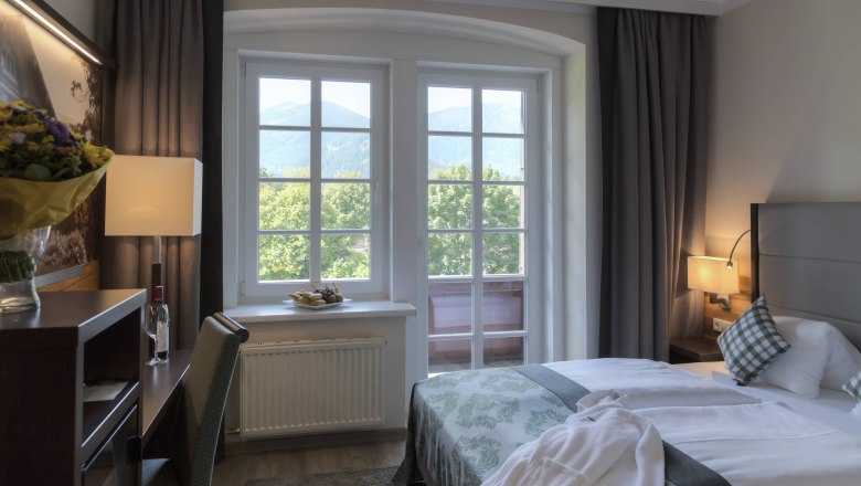 Ein gemütliches Hotelzimmer mit Doppelbett, Fenster mit Bergblick, Schreibtisch und Blumen.