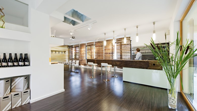 Moderner Verkostungsraum mit Bar, St&uuml;hlen und Weinflaschen.