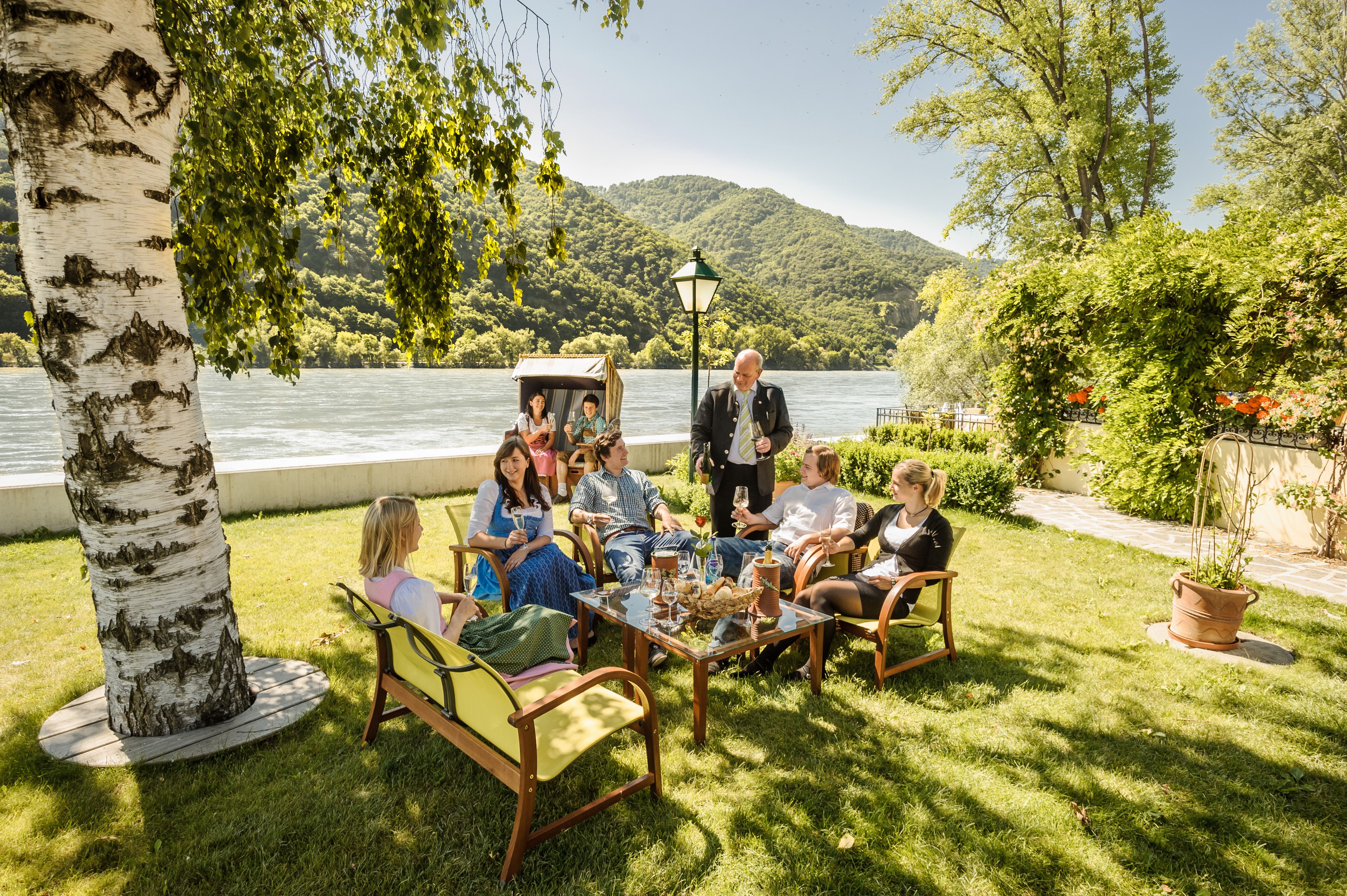 Gruppe von Menschen sitzt im Garten eines Restaurants am Flussufer.