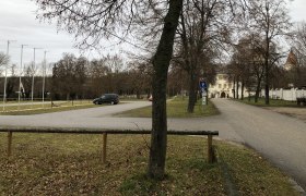 Parkplatz mit Bäumen und einem Gebäude im Hintergrund.