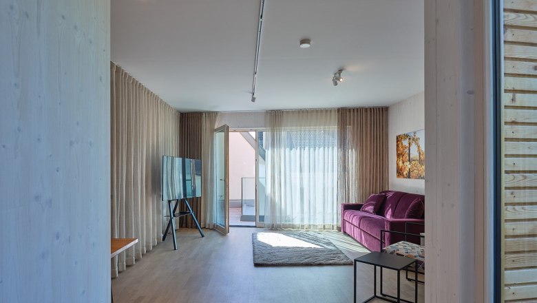 Modernes Wohnzimmer mit lila Sofa, gro&szlig;em Fenster und TV auf St&auml;nder.