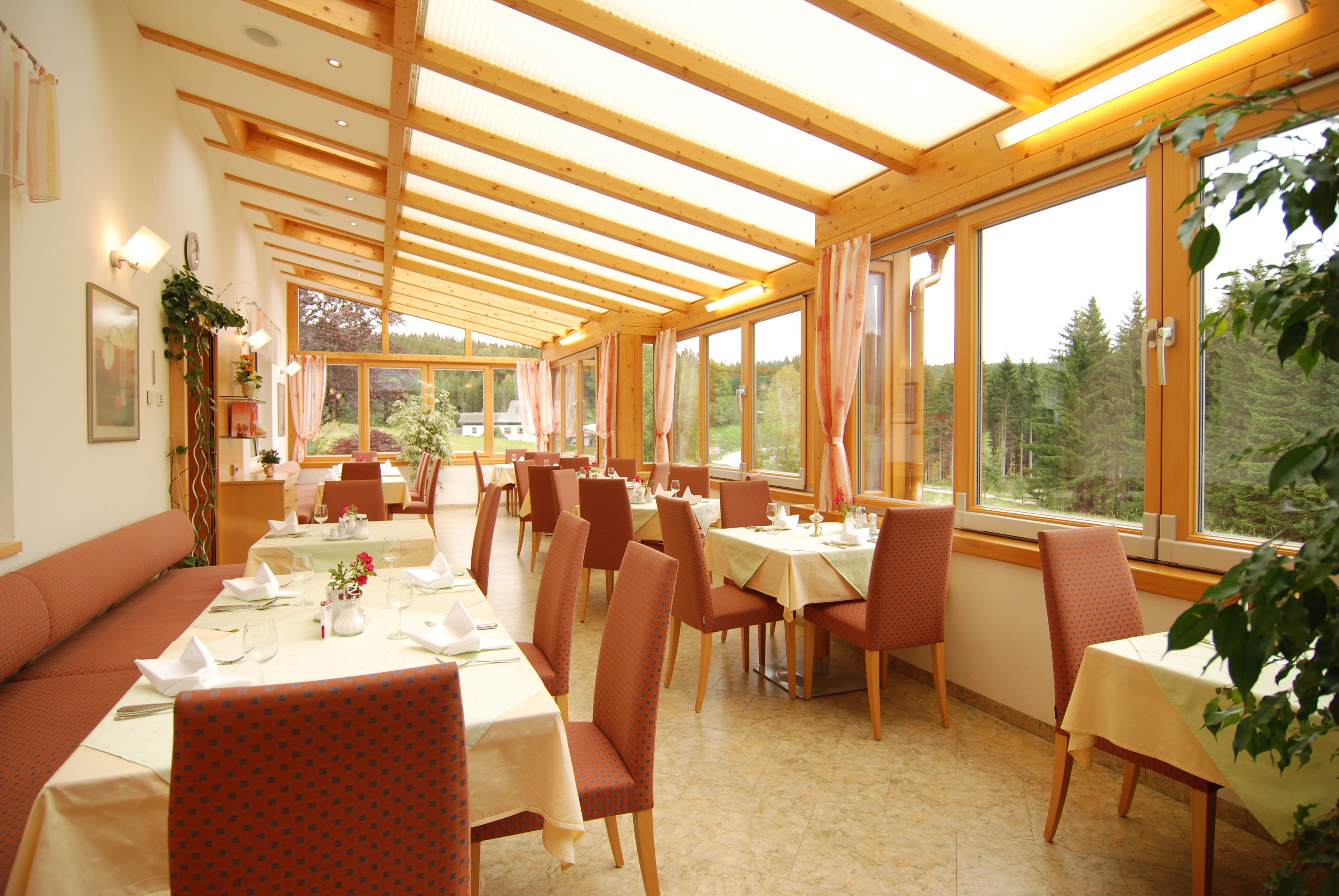Ein heller Wintergarten eines Restaurants mit gedeckten Tischen und Blick auf einen Wald.