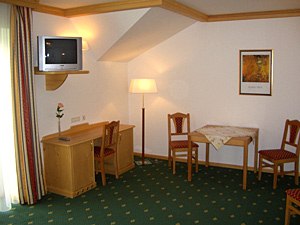 Hotelzimmer mit gr&uuml;nem Teppich, Holzm&ouml;beln, Tisch, St&uuml;hlen und Fernseher.