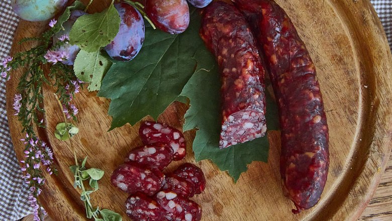 Kaminwurzn und Pflaumen auf einem Holzbrett mit grünen Blättern und Kräutern dekoriert.