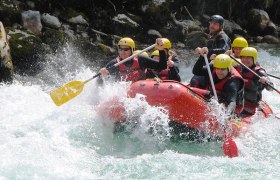 Gruppe beim Rafting auf einem Fluss mit gelben Helmen und roten Westen.