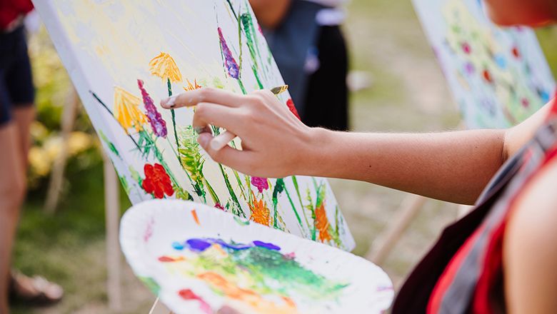 Person malt mit Fingerfarben auf einer Leinwand im Freien.