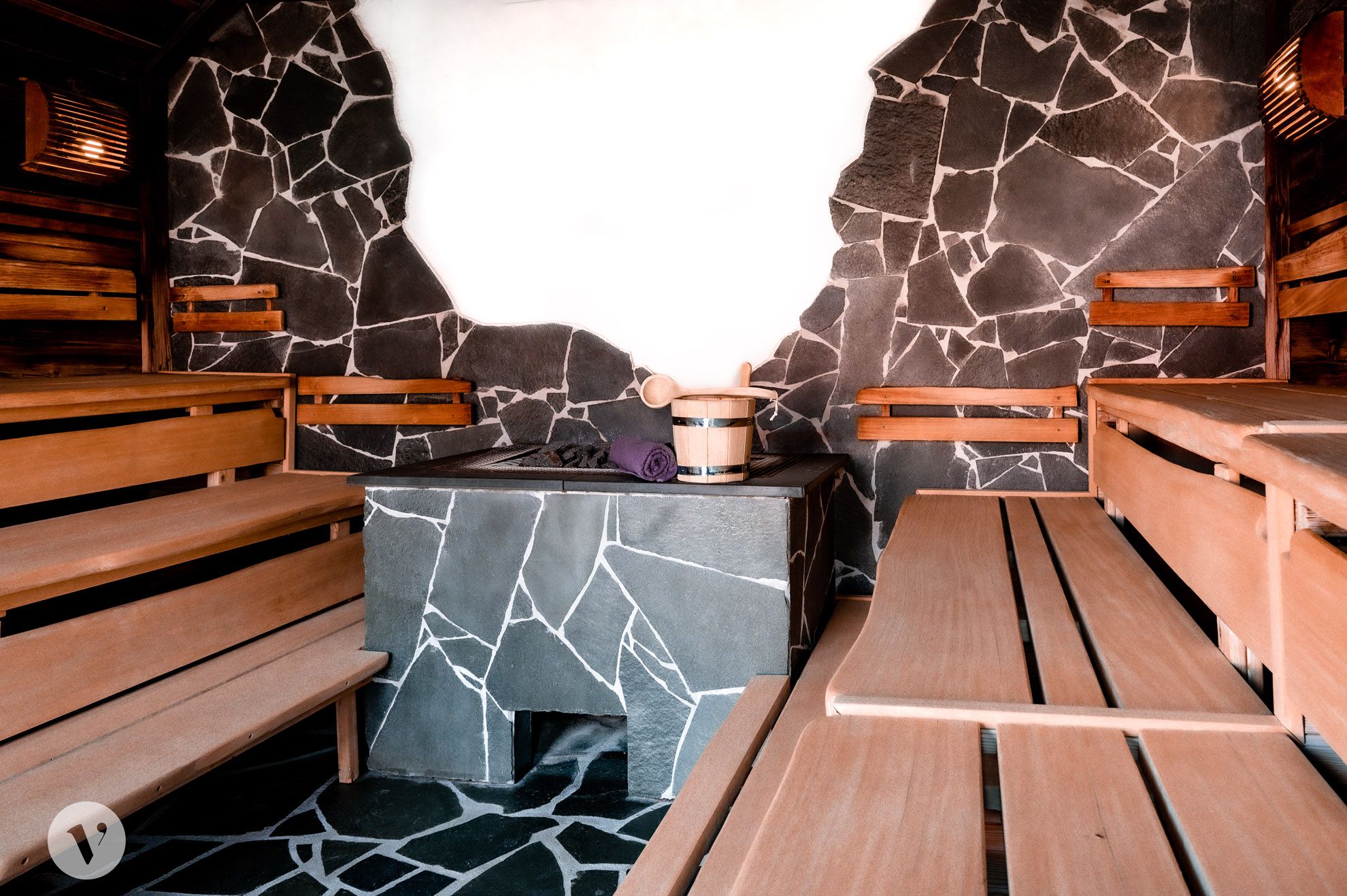 Innenansicht einer Sauna mit Holzbänken und Steinwänden.