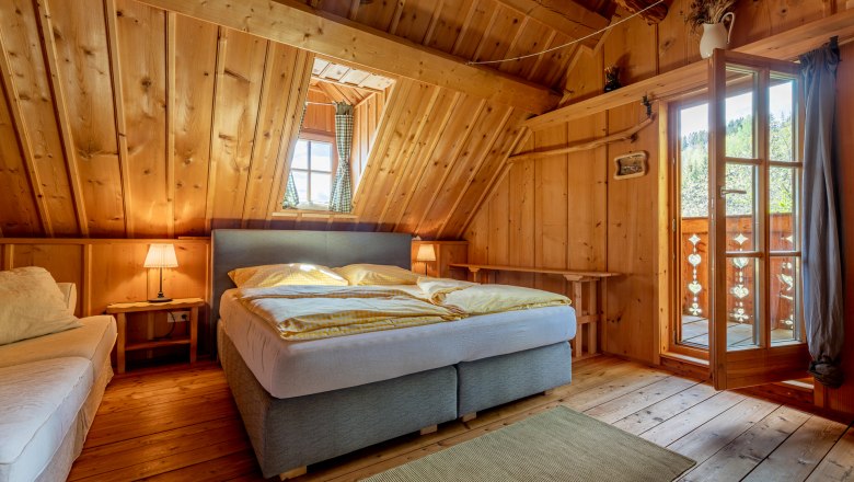Schlafzimmer mit Holzvertäfelung, Doppelbett, Teppich und offener Tür zum Balkon.