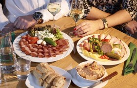 Zwei Personen sitzen an einem Tisch mit Wurst- und K&auml;seplatten, Brot und Wein.