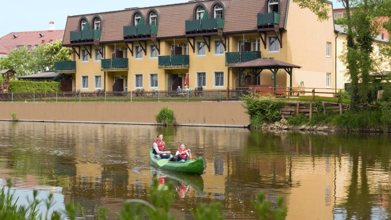 Zwei Personen in einem Kanu auf einem Fluss vor einem gelben Hotel.