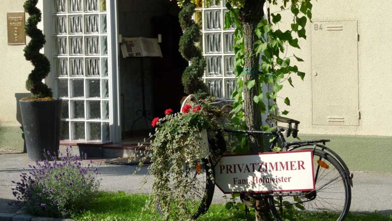 Pension Hofmeister, © Familie Hofmeister Eingang zu einer Pension mit einem dekorierten Fahrrad und einem Schild für Privatzimmer.