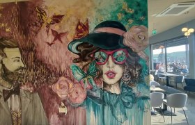 Wandgemälde mit stilisierten Porträts eines Mannes und einer Frau in einem Café.