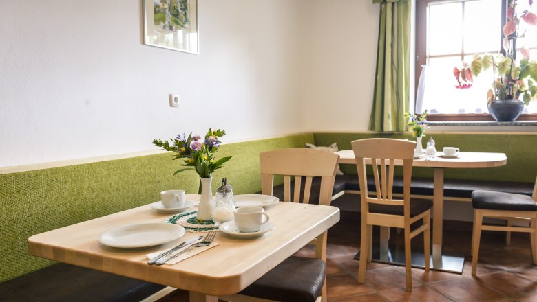 Gem&uuml;tlicher Fr&uuml;hst&uuml;cksraum mit Holztischen, gr&uuml;nen B&auml;nken und Blumen auf dem Tisch.