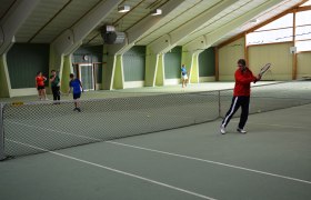 Personen spielen Tennis in einer Tennishalle.