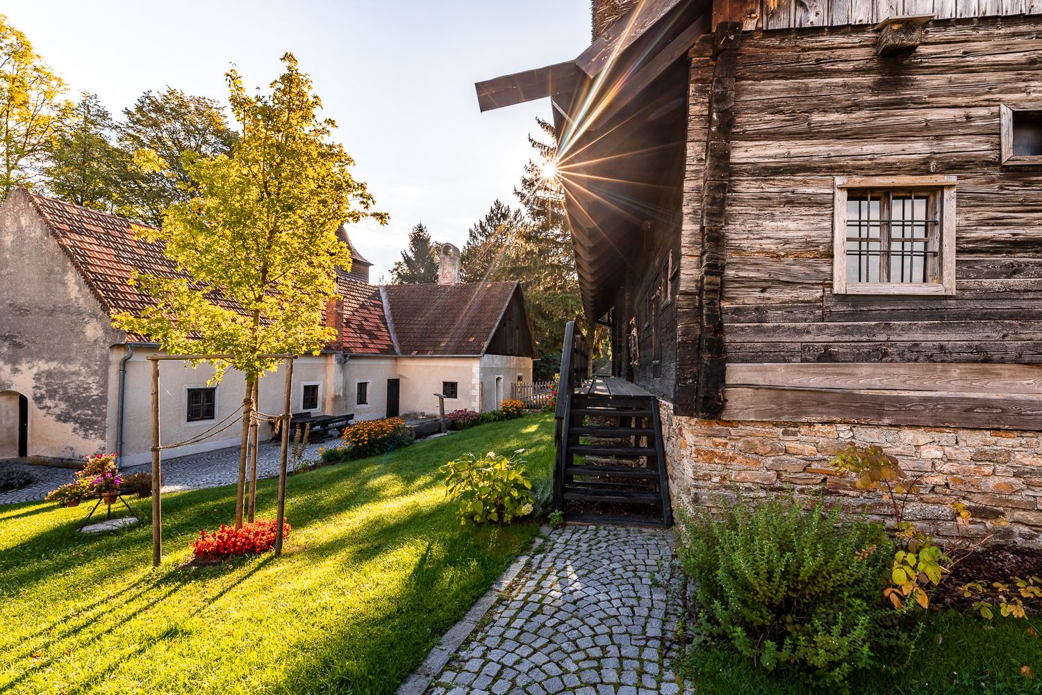 Traditionelle Gebäude und Grünanlage im Museumsdorf Krumbach bei Sonnenuntergang.