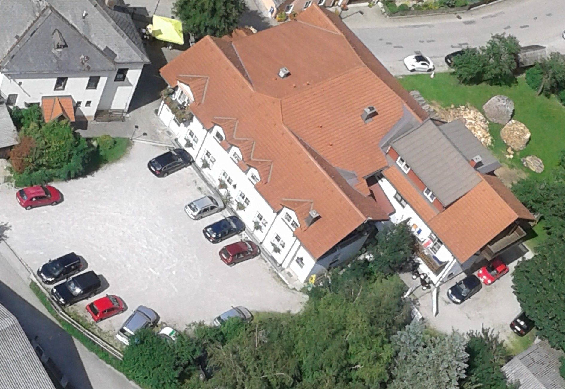 Luftaufnahme eines Gebäudekomplexes mit roten Dächern und mehreren geparkten Autos auf einem Parkplatz.