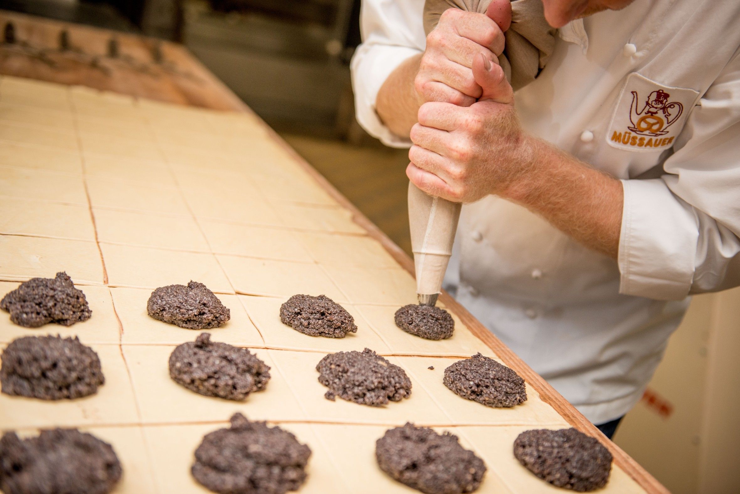 Ein Bäcker spritzt Teig auf ein Backblech in einer Bäckerei.