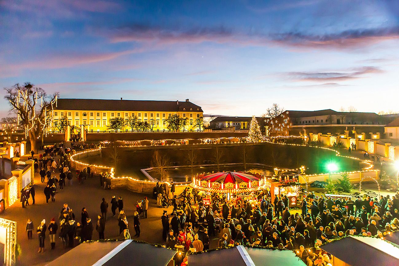 Weihnachtsmarkt im Schloss Hof bei Dämmerung mit Lichtern und Menschen.