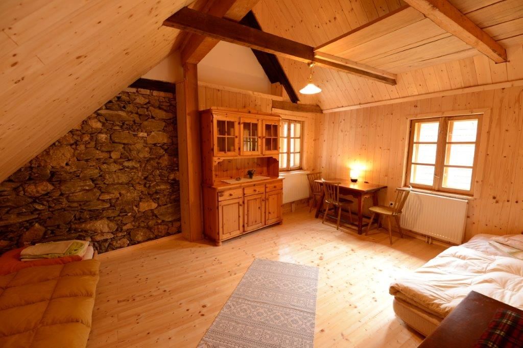 Gemütliches Zimmer mit Holzwänden, zwei Betten, Tisch und Stühlen, Schrank und Steinwand.