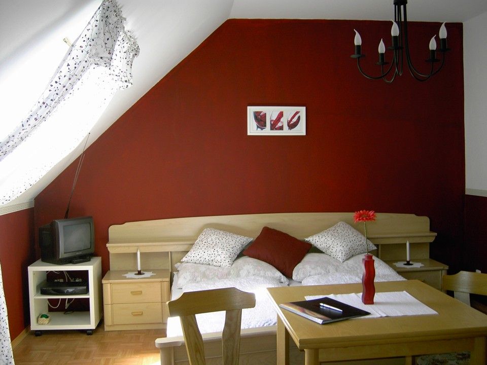 Gemütliches Schlafzimmer mit roter Wand, Bett, Tisch und Fernseher.