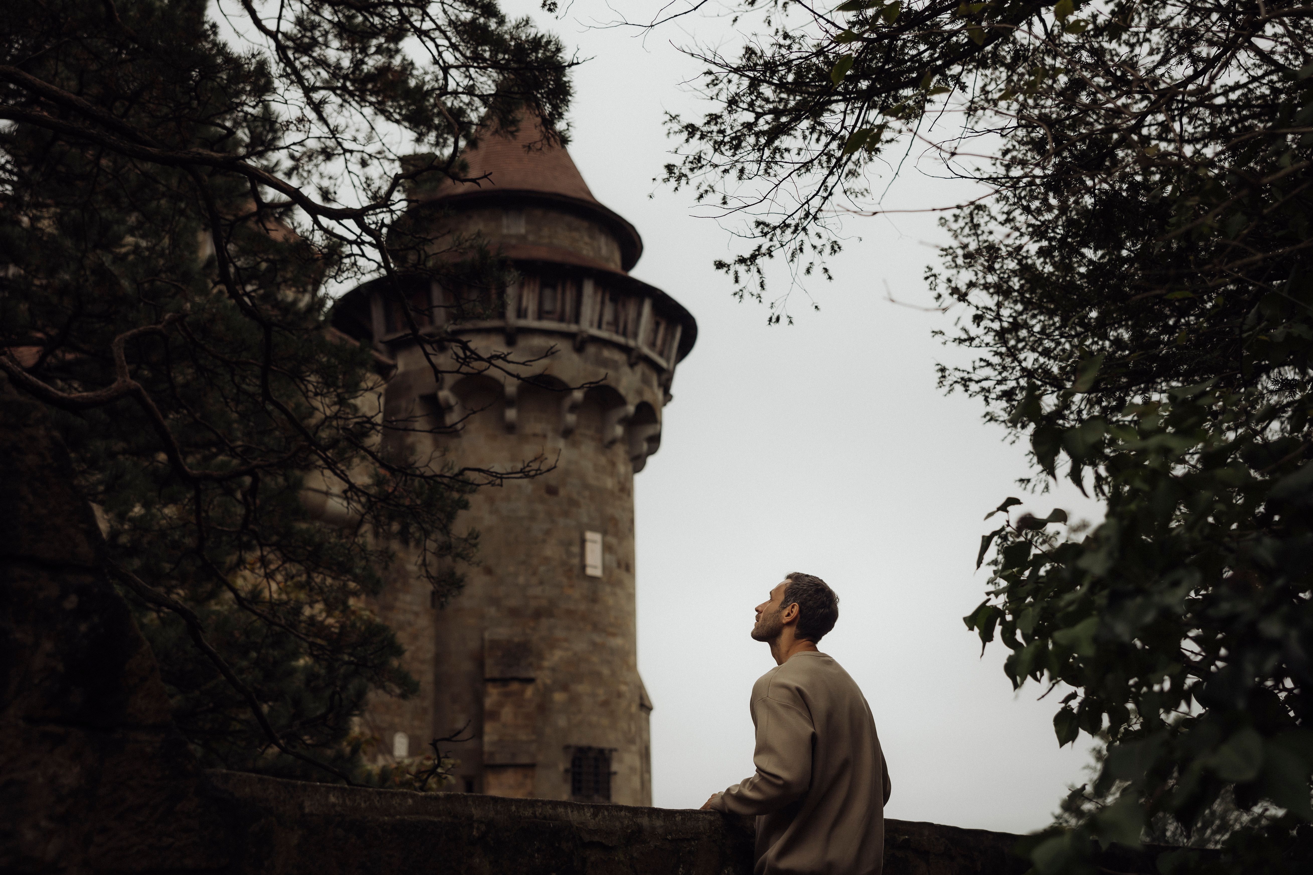 Mann betrachtet Burg Kreuzenstein durch Bäume.