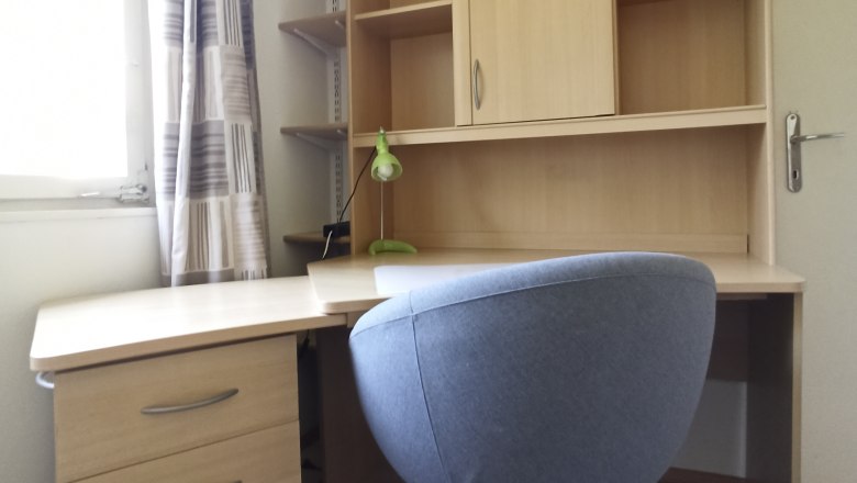 Ein moderner Schreibtisch mit einem grauen B&uuml;rostuhl und einem Regal mit Schubladen und F&auml;chern.