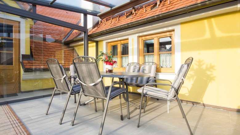 Wintergarten mit Tisch und Stühlen, gelbe Wände, Glasdach.