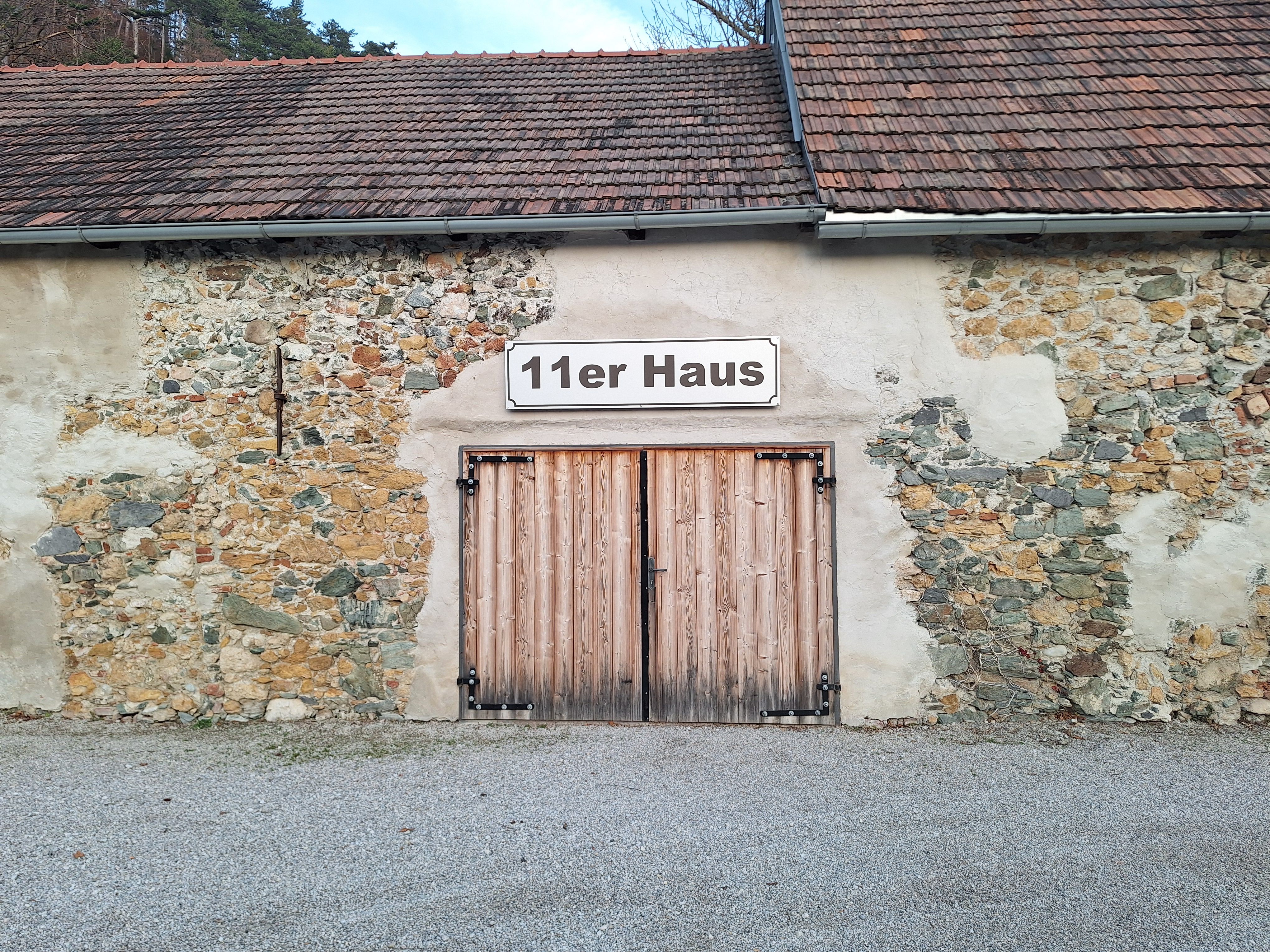 Außenansicht des 11er Hauses mit Holztor und Steinmauer.