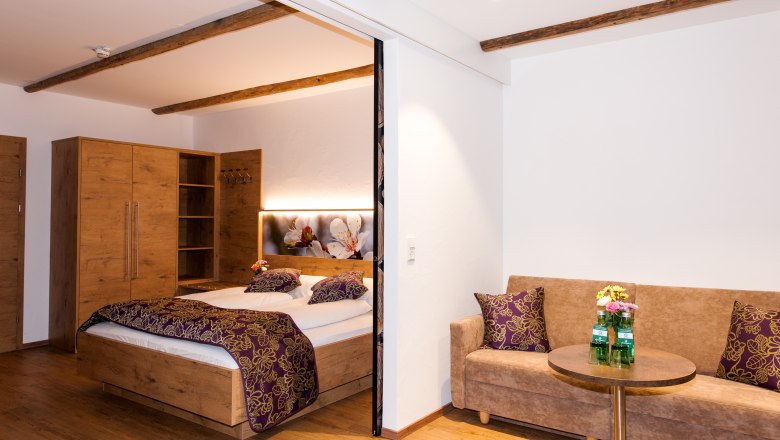 Gemütliches Hotelzimmer mit Holzmöbeln, Doppelbett, Sofa und kleinem Tisch.