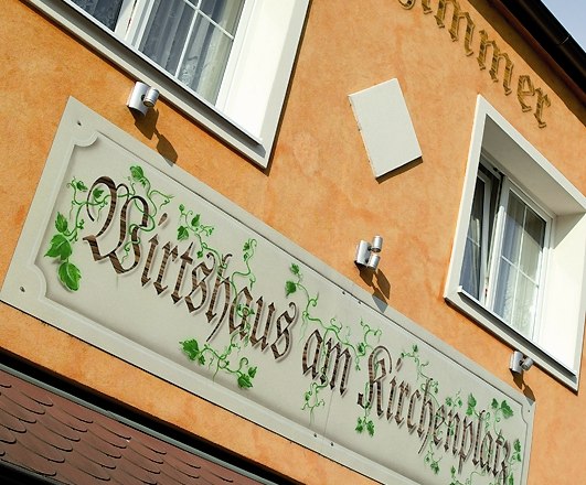 Haus, © Wirtshaus am Kirchenplatz Fassade eines Gebäudes mit dem Schild 'Wirtshaus am Kirchenplatz'.