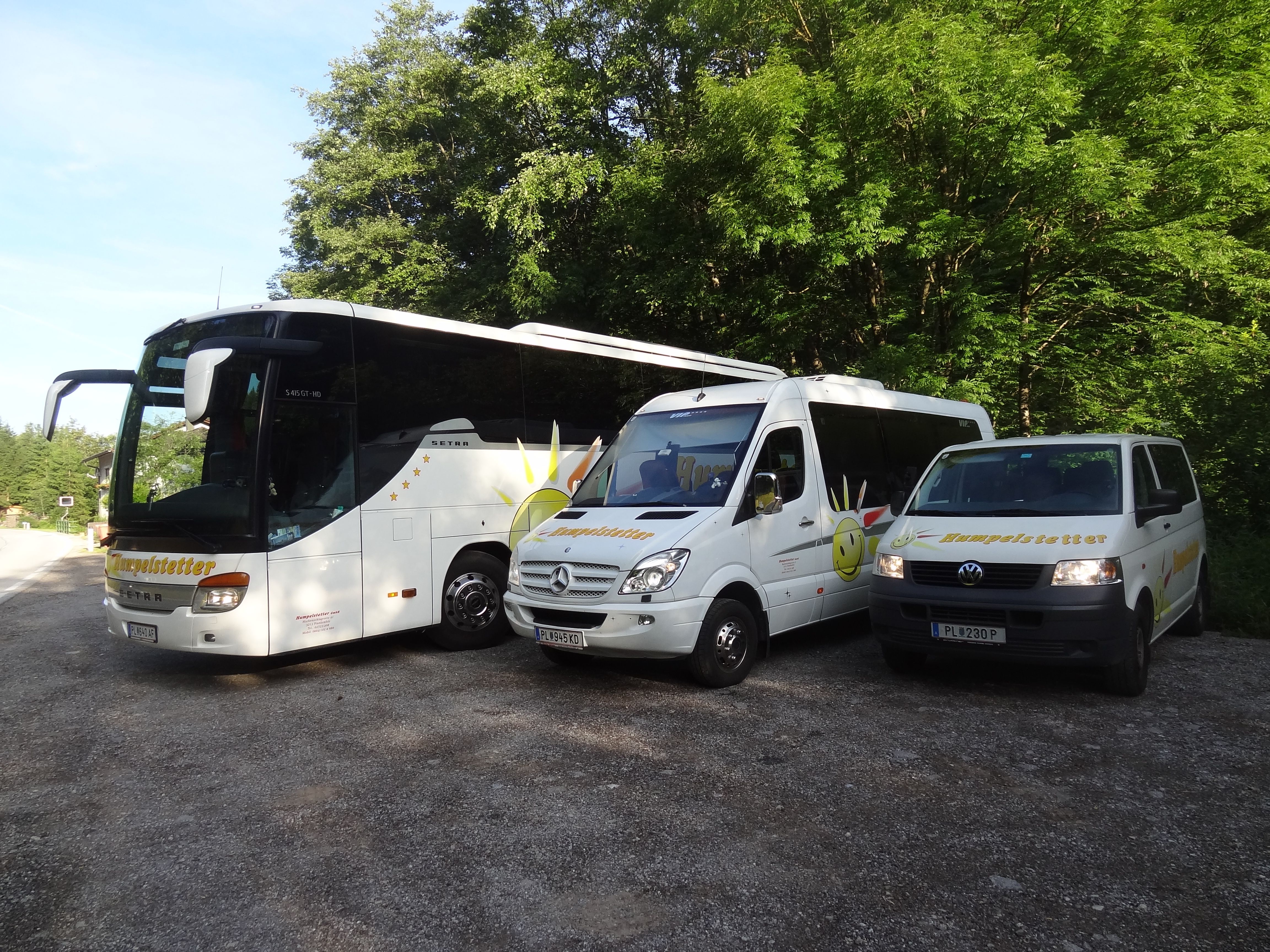 Drei weiße Fahrzeuge mit Humpelstetter-Logo, geparkt auf einem Schotterplatz vor Bäumen.