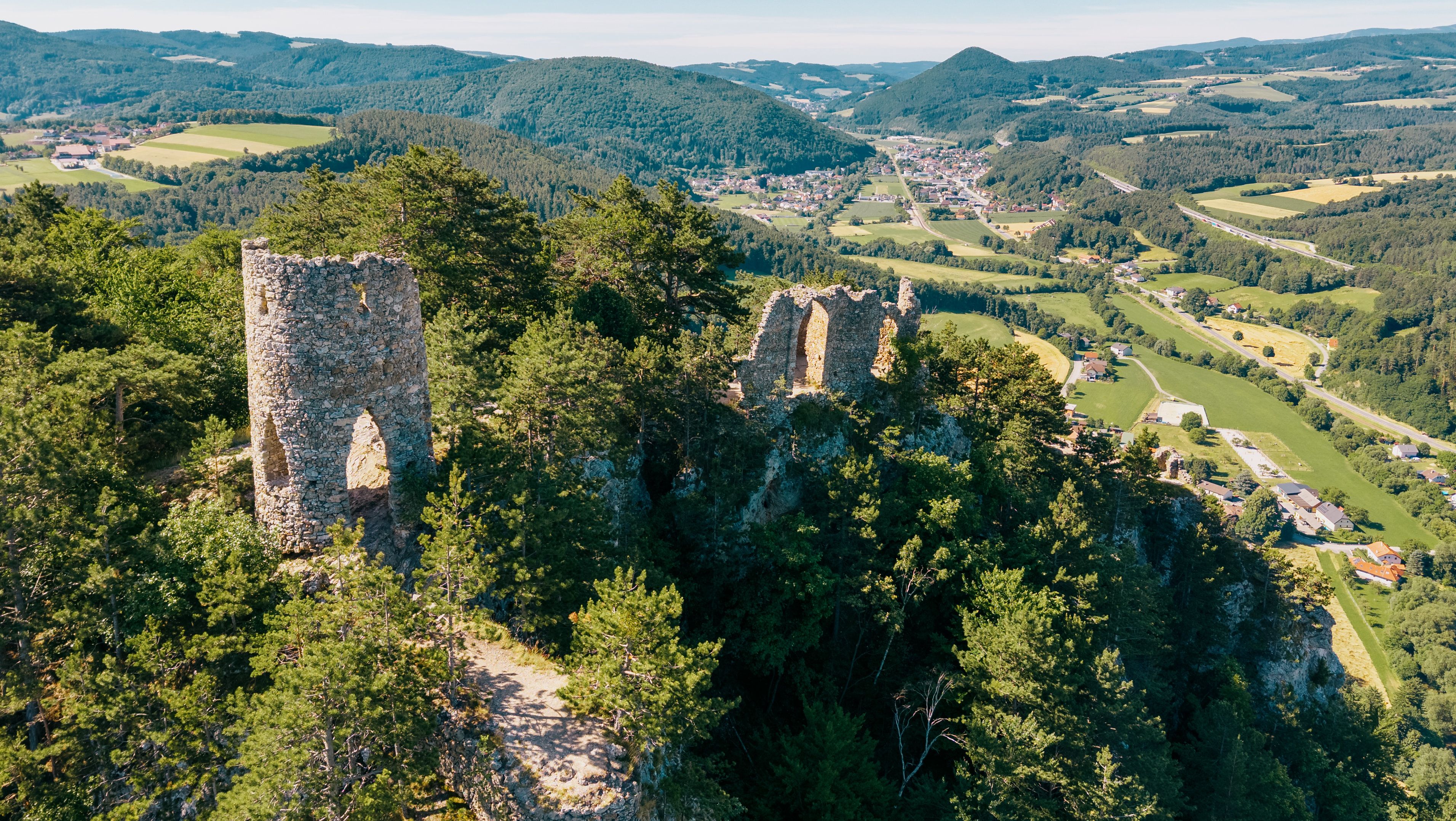 Luftaufnahme der Ruine Türkensturz inmitten von bewaldeten Hügeln und grünen Tälern.
