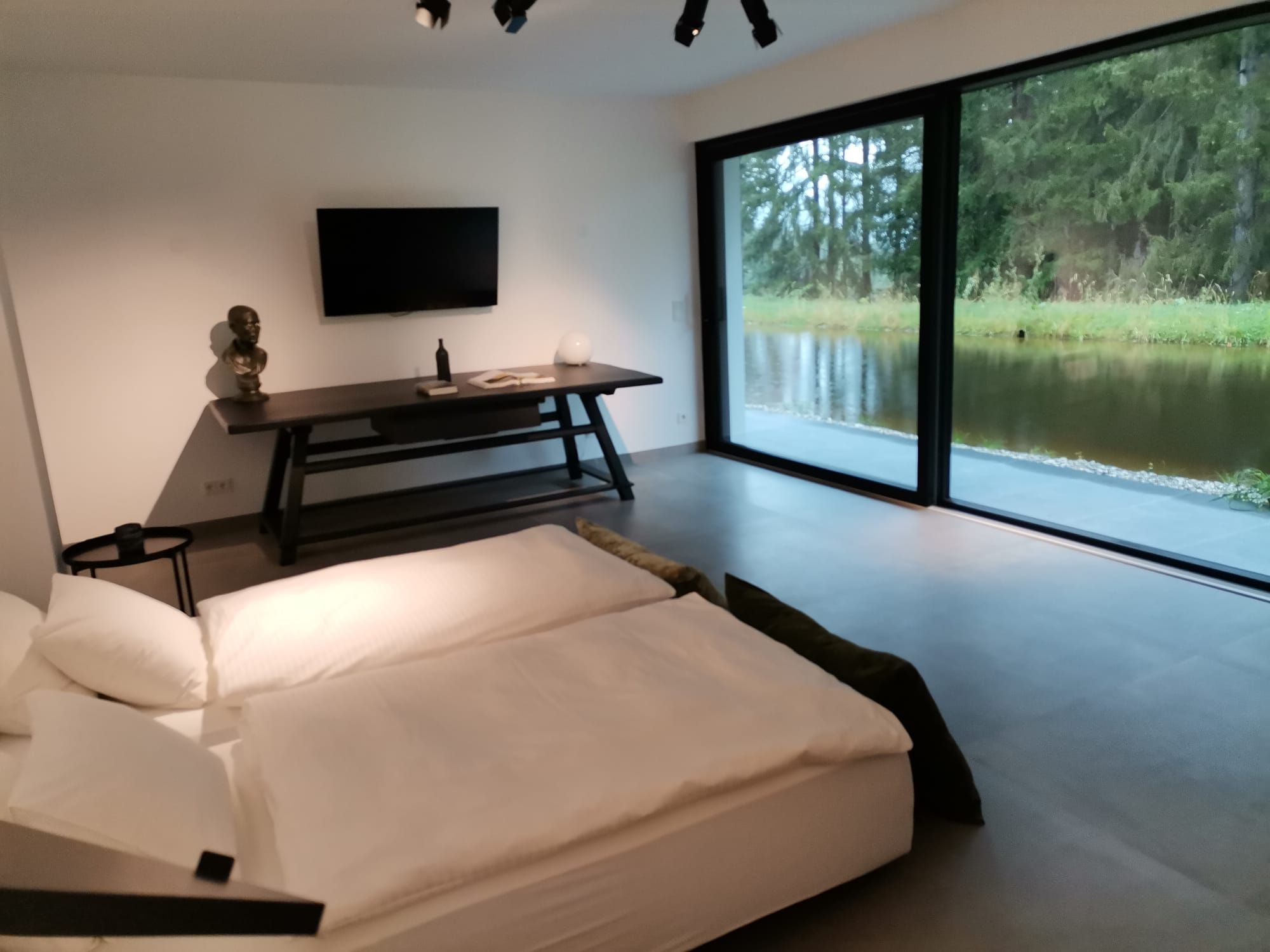 Modernes Schlafzimmer mit großem Fenster und Blick auf einen Teich.