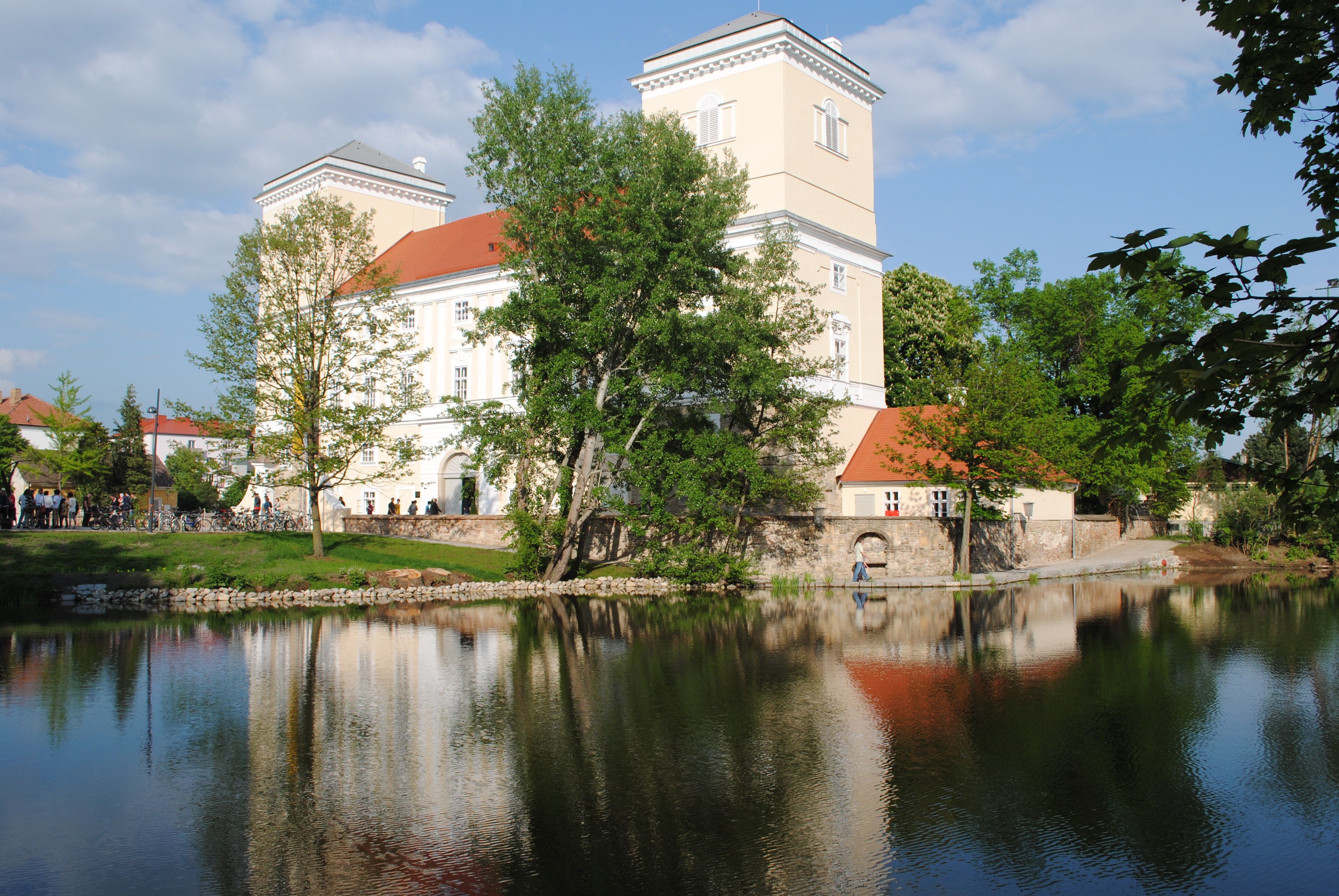Schloss Wolkersdorf mit Spiegelung im Wasser und umgeben von Bäumen.