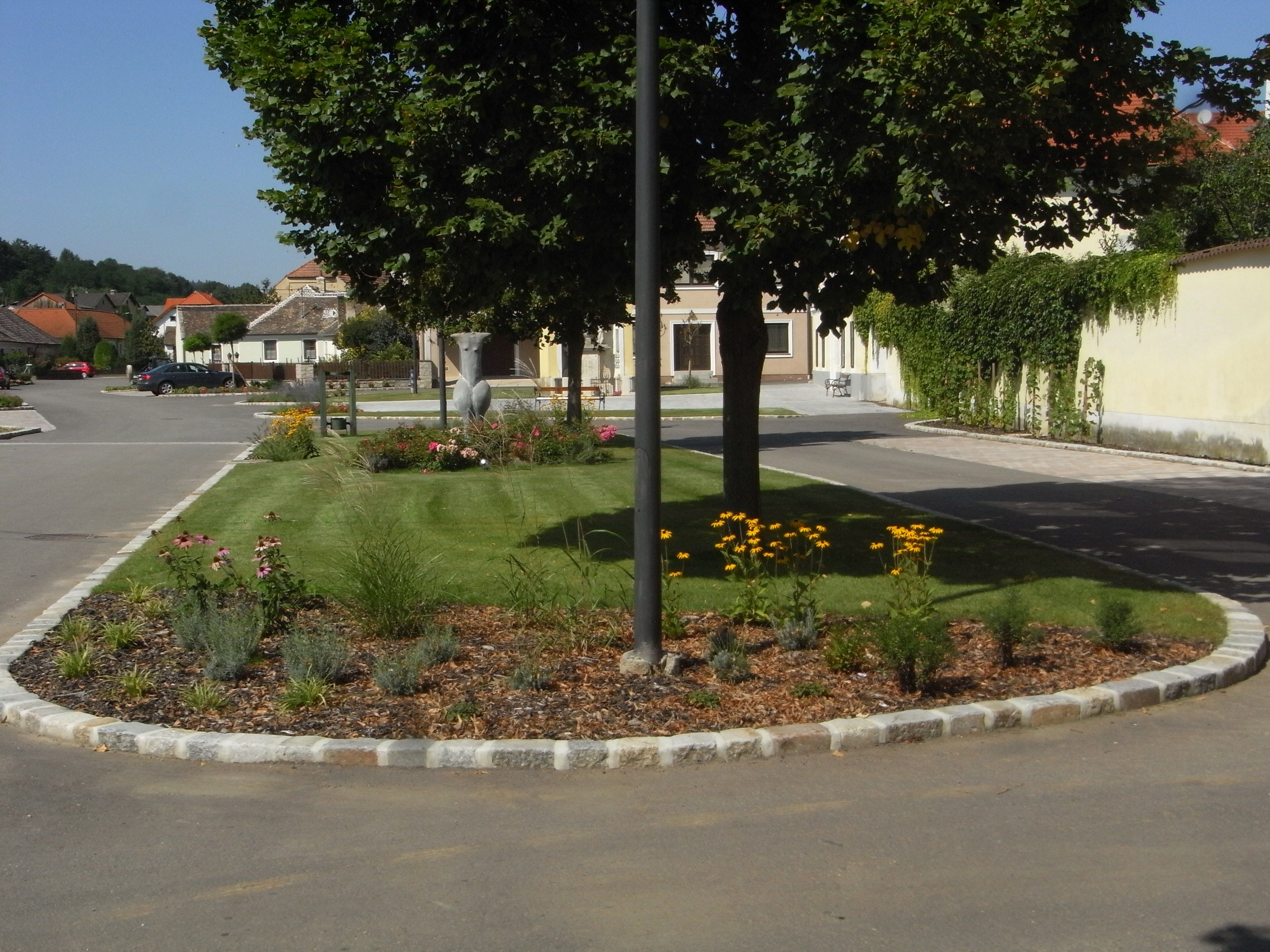 Ein gepflegtes Blumenbeet mit gelben Blumen und Bäumen in einer ruhigen Wohnstraße.