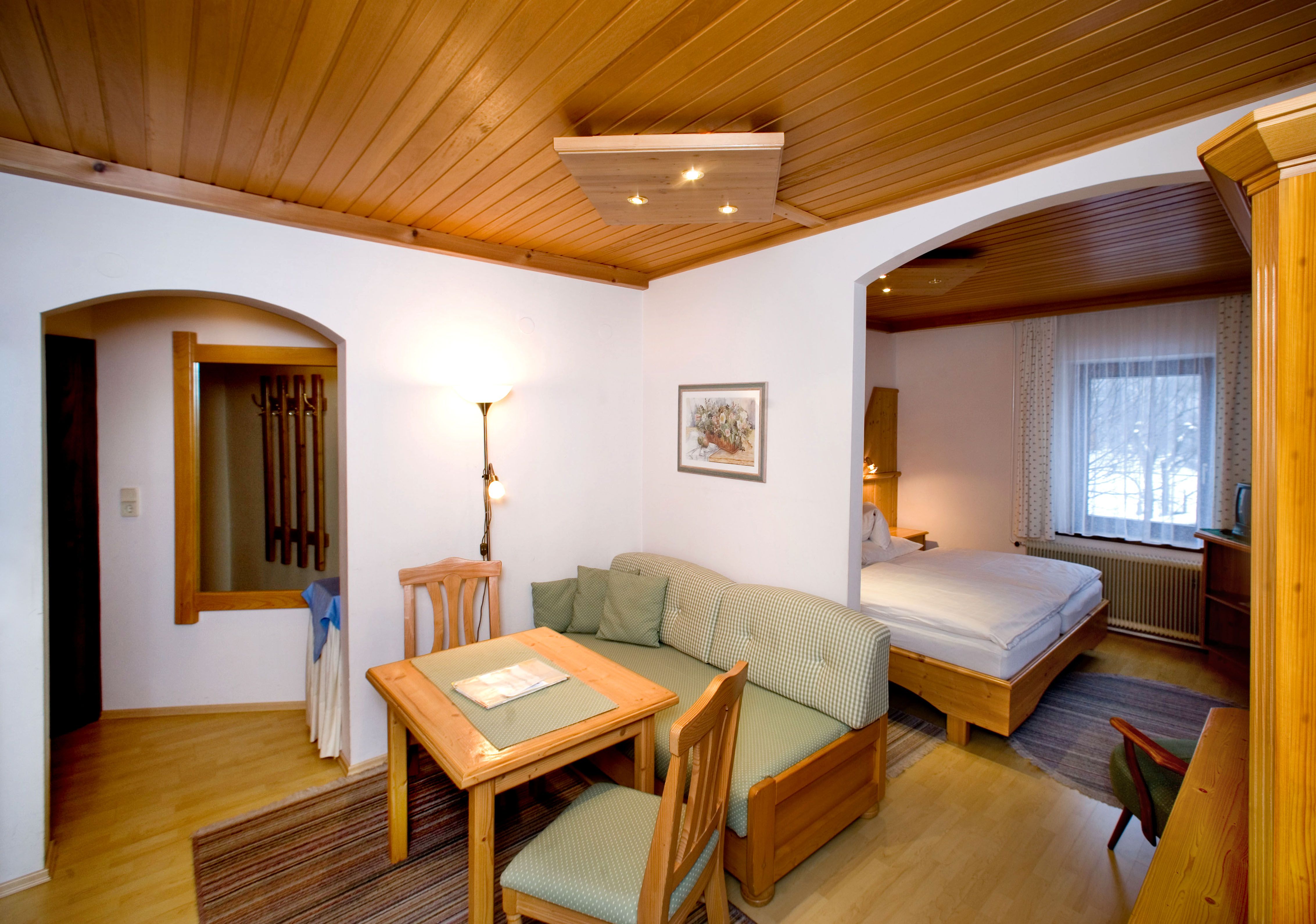 Gemütliches Hotelzimmer mit Holzmöbeln, Esstisch, Sofa und Doppelbett.