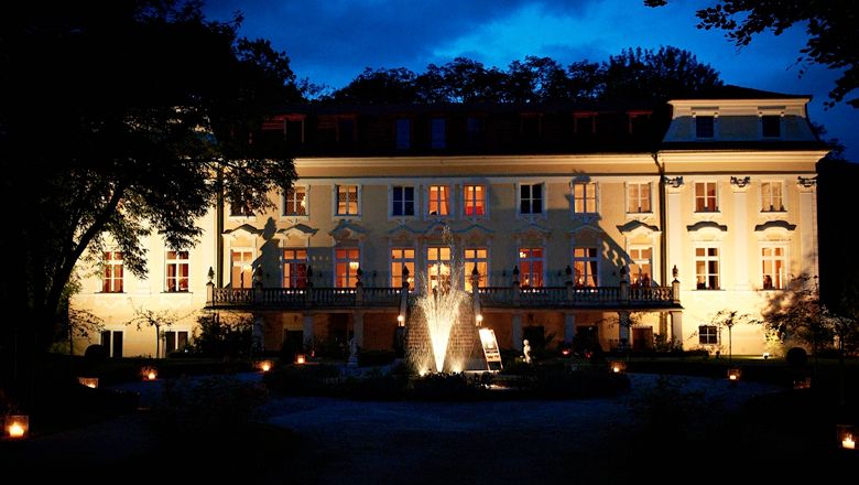 Beleuchtetes Schloss Stuppach bei Nacht mit Springbrunnen im Vordergrund.