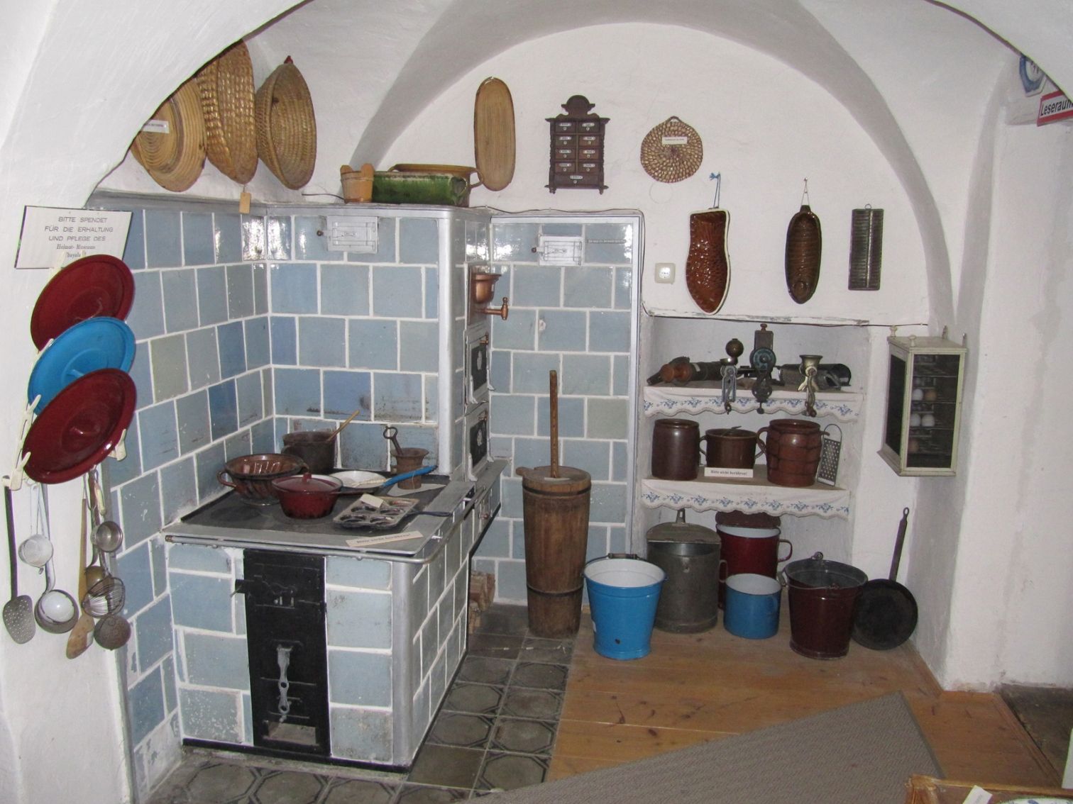 Historische Küche mit blau gefliestem Herd und alten Küchenutensilien.