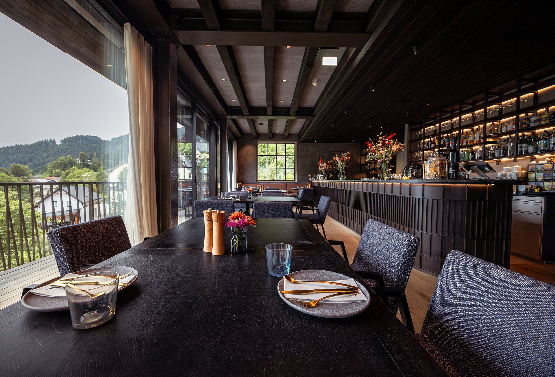 In einem stilvollen Restaurant mit Blick auf die umliegenden Berge genießen Gäste eine einladende Atmosphäre. Die eleganten Tische sind liebevoll gedeckt und laden dazu ein, die kulinarischen Köstlichkeiten der Region zu probieren. Große Fenster lassen das Licht herein und bieten einen atemberaubenden Ausblick auf die Natur.