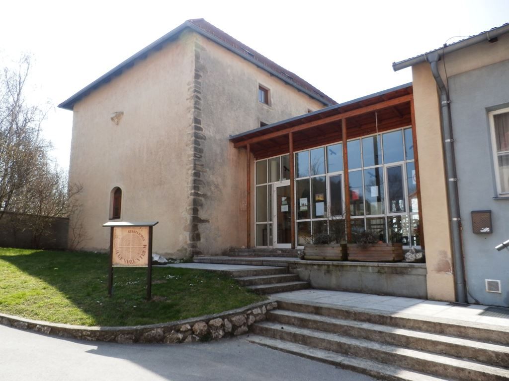 Ein historisches Gebäude mit modernem Anbau und einem Schild im Vordergrund.