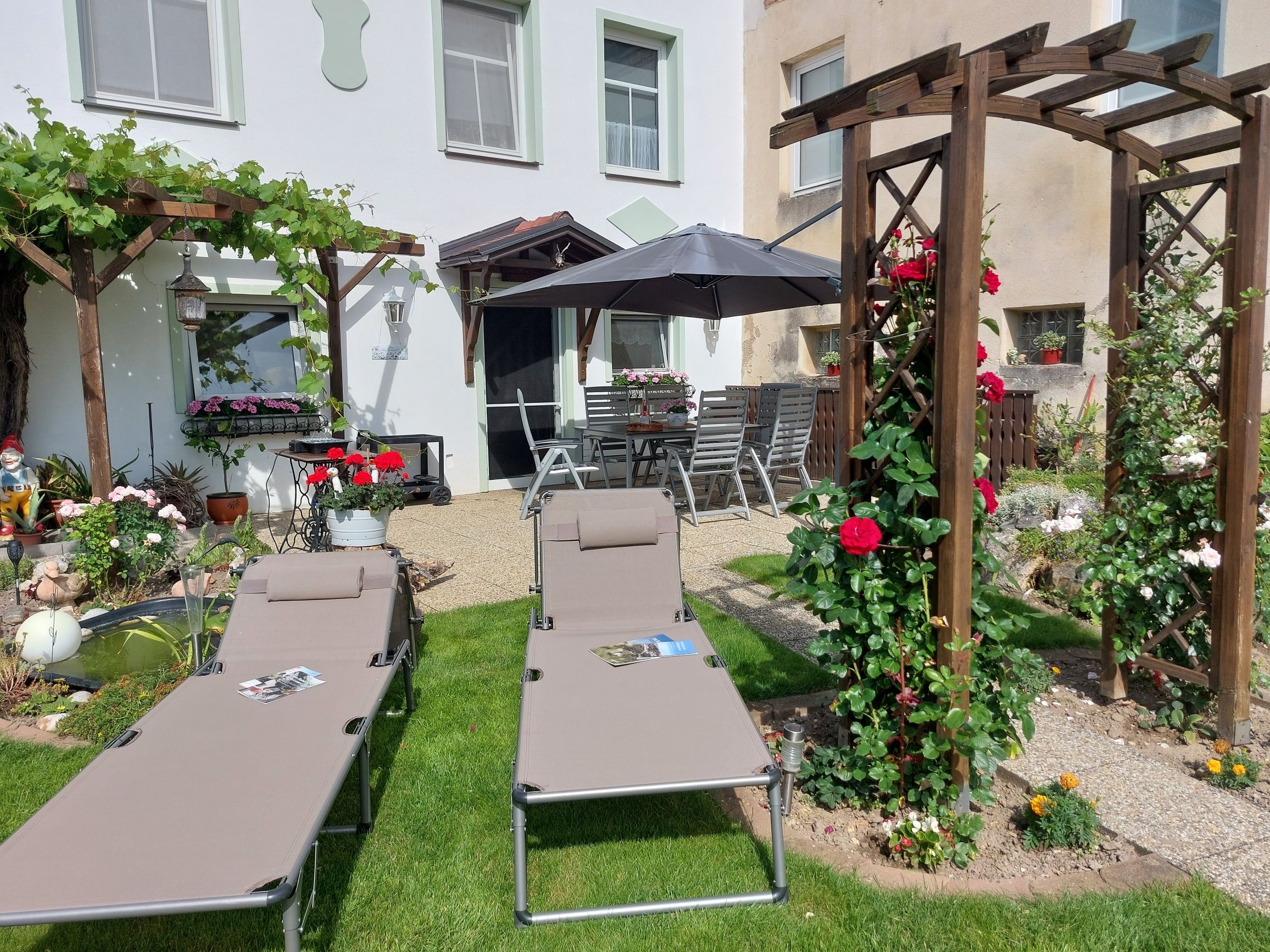Garten mit Liegestühlen, Pergola und Blumen.