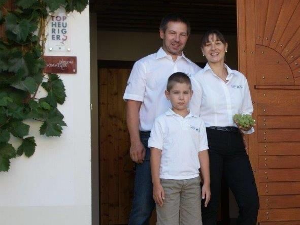 Eine Familie steht vor einem Gebäude mit Holztür, die Frau hält Trauben.