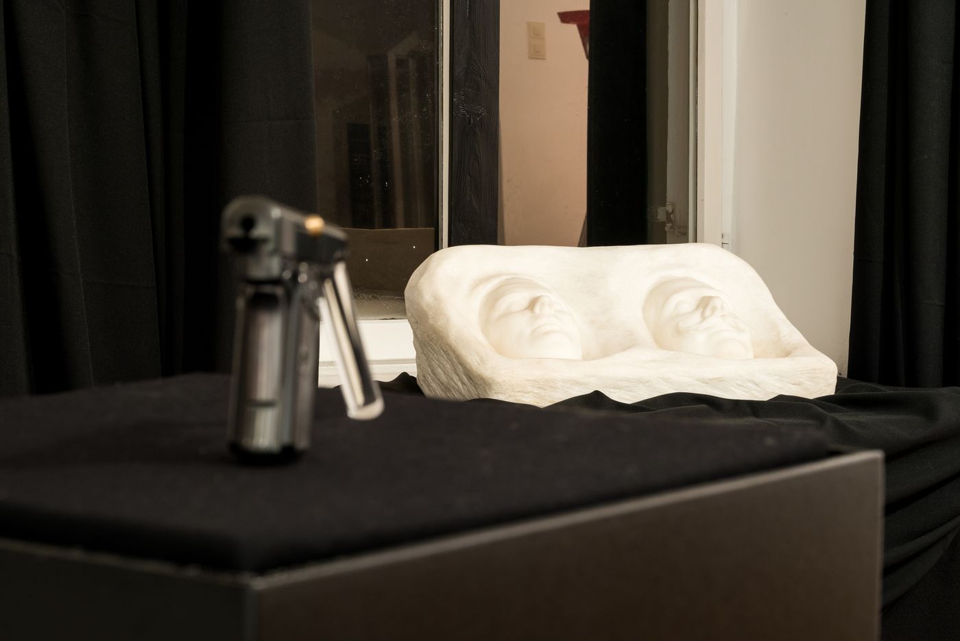 Skulptur mit zwei Gesichtern und unscharfem Objekt im Vordergrund.